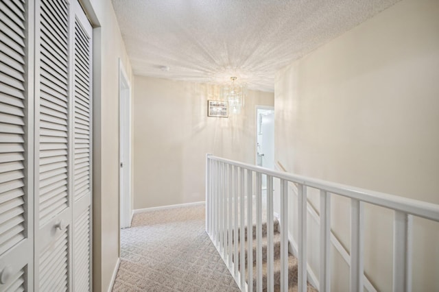 hallway with light colored carpet, a textured ceiling, and an inviting chandelier