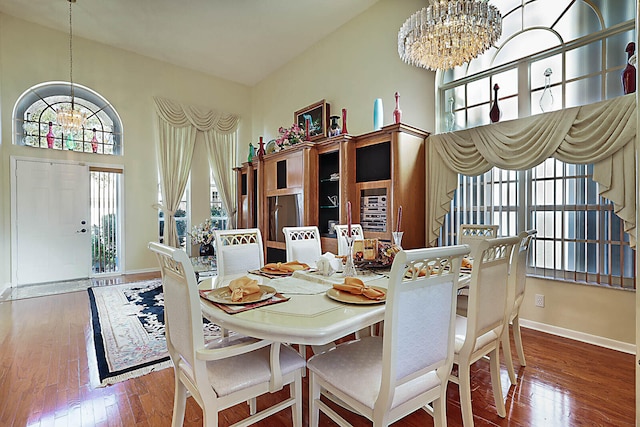 dining area with hardwood / wood-style flooring, a towering ceiling, and an inviting chandelier