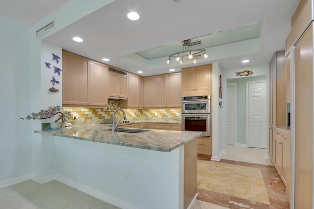 kitchen featuring tasteful backsplash, a sink, double oven, a raised ceiling, and a peninsula
