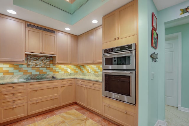 kitchen with light brown cabinets, black electric cooktop, double oven, and light stone countertops