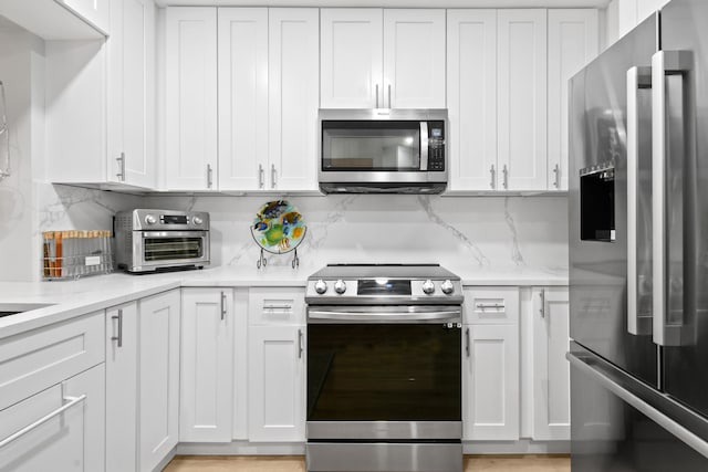 kitchen with light stone counters, stainless steel appliances, tasteful backsplash, and white cabinetry