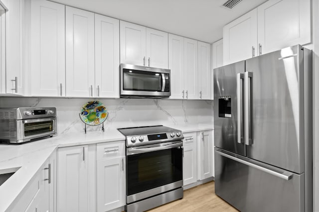 kitchen featuring light wood-type flooring, tasteful backsplash, white cabinetry, appliances with stainless steel finishes, and light stone countertops