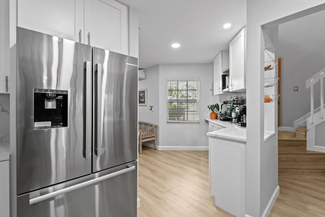 kitchen with stainless steel fridge, light hardwood / wood-style floors, light stone countertops, and white cabinets