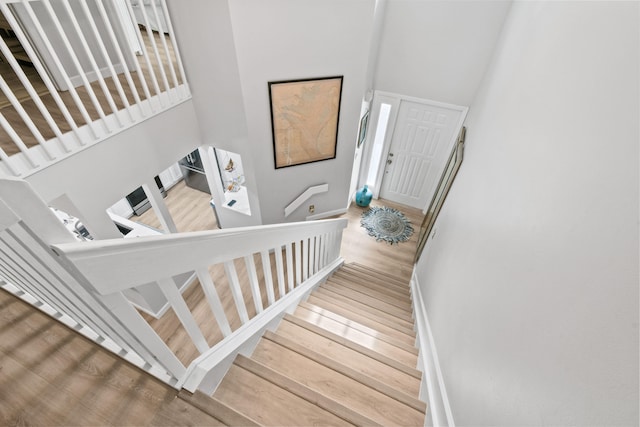 stairway with wood-type flooring and a towering ceiling