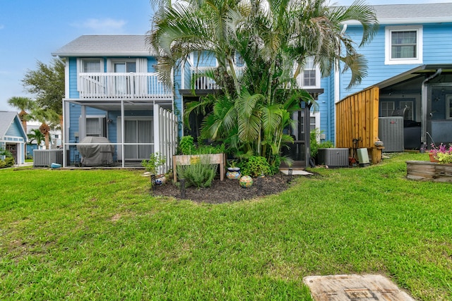 rear view of property featuring a balcony, a sunroom, a lawn, and central AC