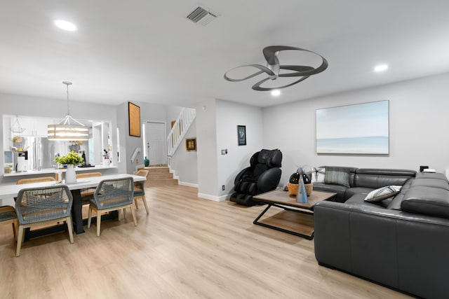 living room with ceiling fan with notable chandelier and light hardwood / wood-style floors