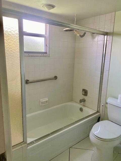 bathroom featuring combined bath / shower with glass door, tile patterned floors, and toilet