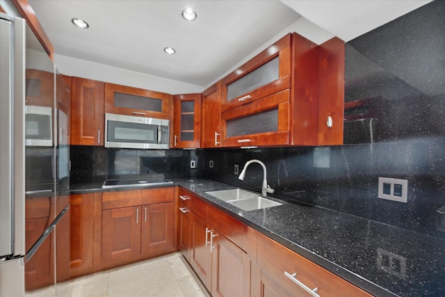 kitchen featuring stainless steel appliances, backsplash, brown cabinetry, a sink, and dark stone counters