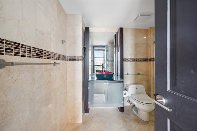 bathroom featuring visible vents, toilet, tile patterned floors, vanity, and tile walls