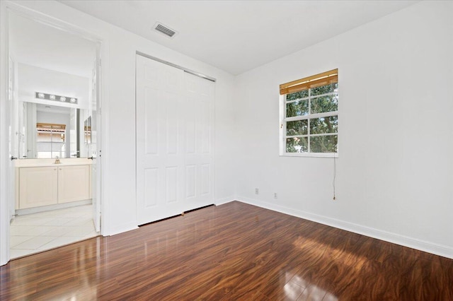 unfurnished bedroom featuring connected bathroom, a closet, and wood-type flooring