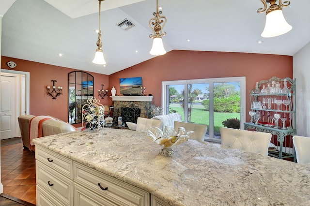 kitchen with light stone counters, cream cabinets, decorative light fixtures, a fireplace, and lofted ceiling