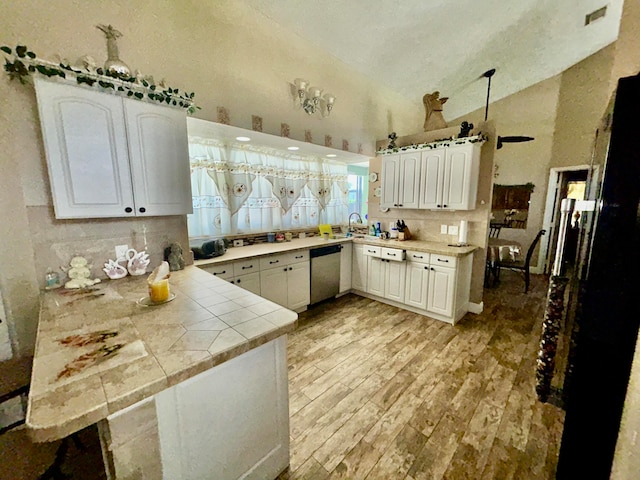 kitchen featuring kitchen peninsula, stainless steel dishwasher, vaulted ceiling, light hardwood / wood-style flooring, and white cabinetry