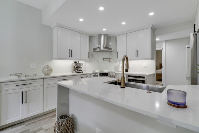 kitchen featuring white cabinetry, stainless steel appliances, wall chimney range hood, and light hardwood / wood-style flooring