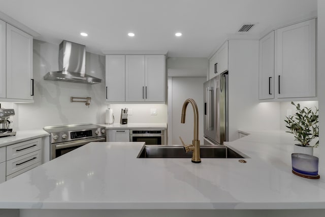 kitchen with wall chimney range hood, white cabinets, sink, and appliances with stainless steel finishes