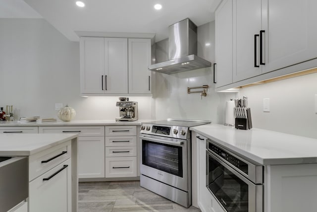 kitchen featuring wall chimney exhaust hood, white cabinetry, stainless steel appliances, and light wood-type flooring