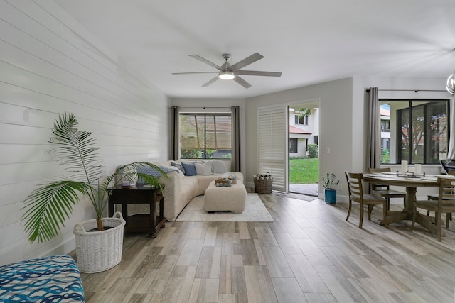 living room featuring light hardwood / wood-style floors, wooden walls, and ceiling fan