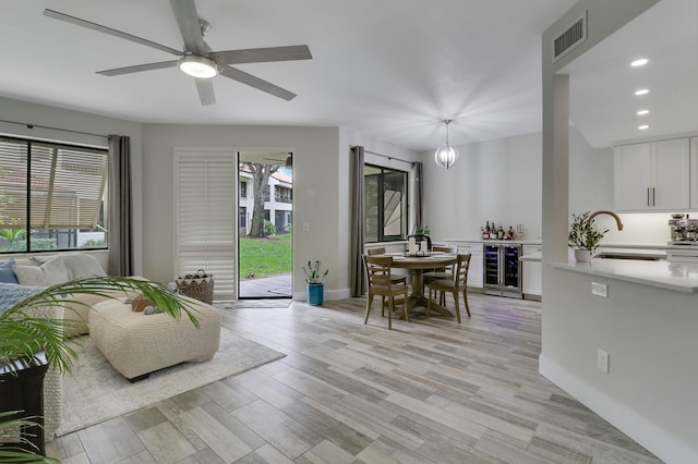 living room featuring light hardwood / wood-style floors, sink, ceiling fan with notable chandelier, and beverage cooler