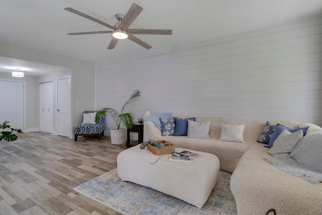 living room featuring ceiling fan, light hardwood / wood-style flooring, and wooden walls