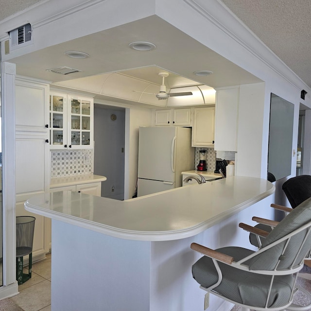 kitchen with kitchen peninsula, white cabinetry, a breakfast bar area, and white refrigerator