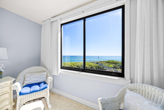 living area with a textured ceiling, a water view, and carpet flooring