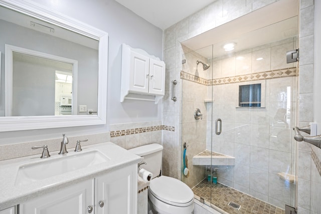 bathroom featuring tile walls, vanity, toilet, and an enclosed shower