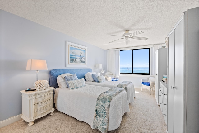 bedroom with a water view, ceiling fan, light colored carpet, and a textured ceiling