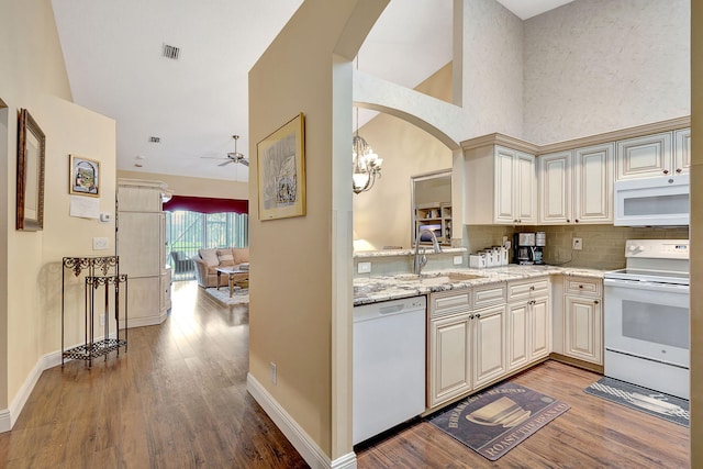 kitchen with ceiling fan with notable chandelier, white appliances, light stone countertops, hardwood / wood-style floors, and sink