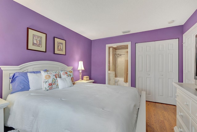 bedroom featuring a textured ceiling, light hardwood / wood-style flooring, ensuite bath, and a closet