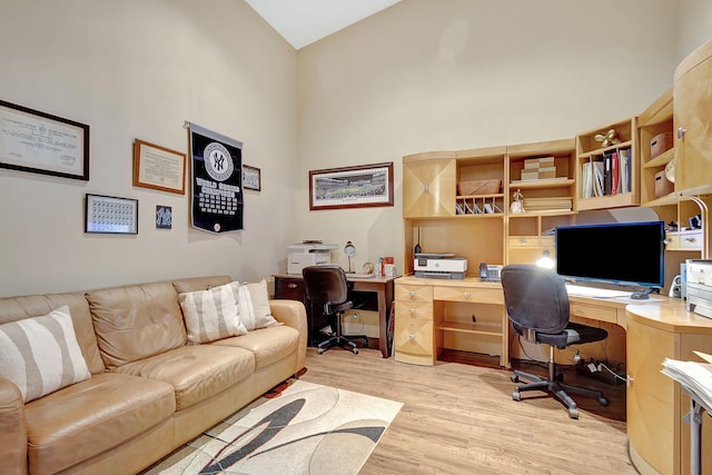 office featuring light wood-type flooring, built in desk, and high vaulted ceiling