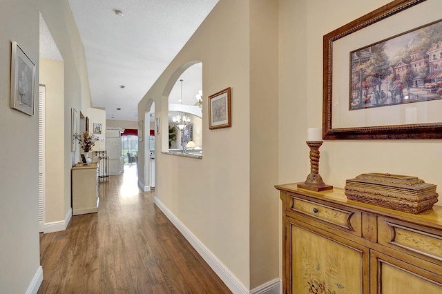 corridor featuring dark wood-type flooring, a chandelier, and a textured ceiling