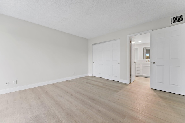 unfurnished bedroom with a textured ceiling, connected bathroom, a closet, and light hardwood / wood-style floors