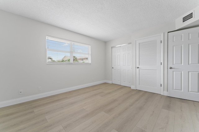 unfurnished bedroom featuring light hardwood / wood-style floors, multiple closets, and a textured ceiling