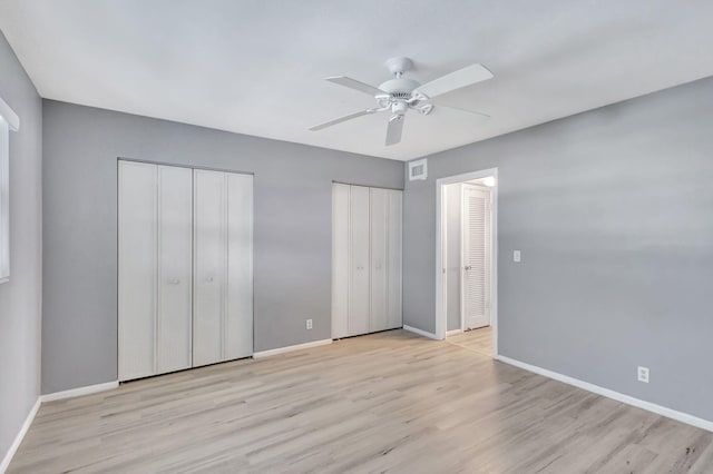 unfurnished bedroom with light hardwood / wood-style flooring, ceiling fan, and two closets