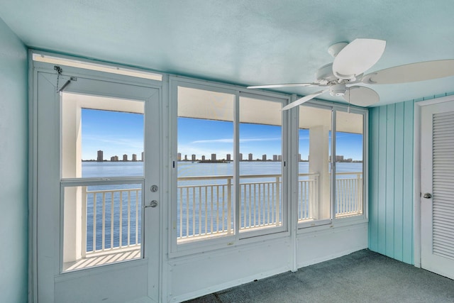 unfurnished sunroom with ceiling fan and a water view