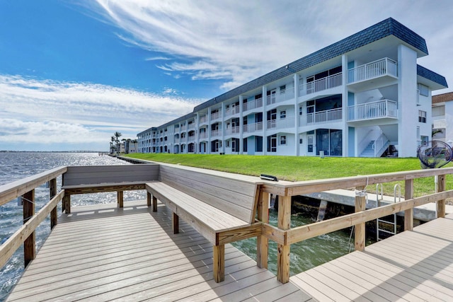 view of dock with a water view, a yard, and a balcony