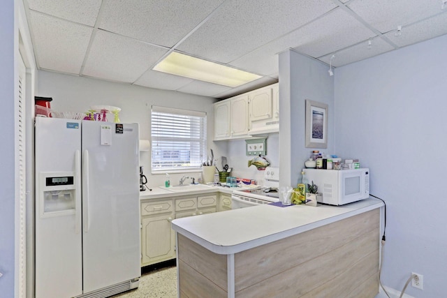 kitchen featuring kitchen peninsula, sink, white appliances, and a drop ceiling