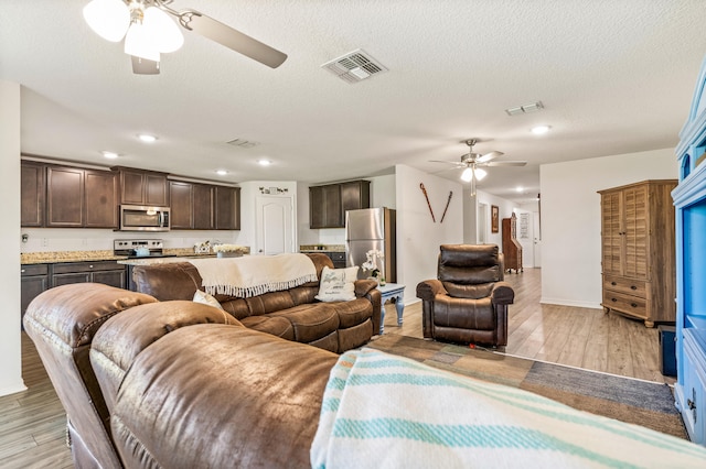 living room with light wood-type flooring, ceiling fan, and a textured ceiling