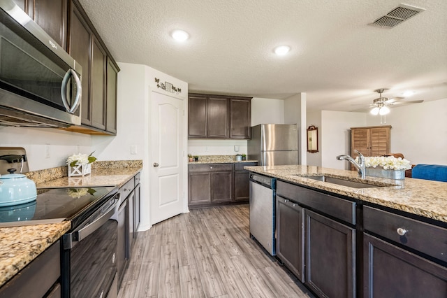 kitchen with a textured ceiling, stainless steel appliances, sink, ceiling fan, and light wood-type flooring