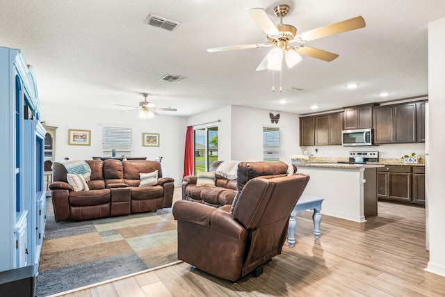 living room featuring a textured ceiling, ceiling fan, and light wood-type flooring