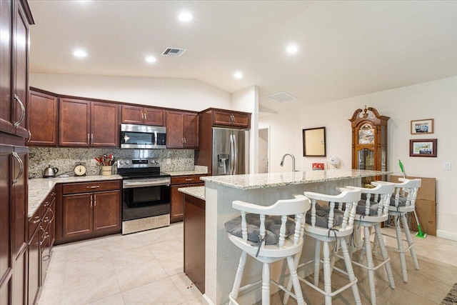 kitchen with a kitchen breakfast bar, stainless steel appliances, an island with sink, and light stone countertops