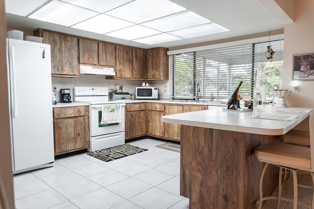 kitchen featuring white appliances, a kitchen bar, kitchen peninsula, sink, and light tile patterned flooring