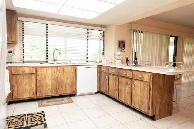 kitchen featuring dishwasher, sink, kitchen peninsula, light tile patterned flooring, and a kitchen breakfast bar