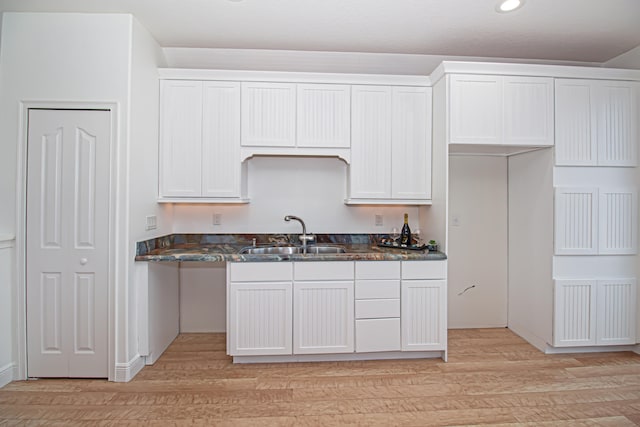 kitchen featuring sink, white cabinets, light hardwood / wood-style floors, and dark stone counters