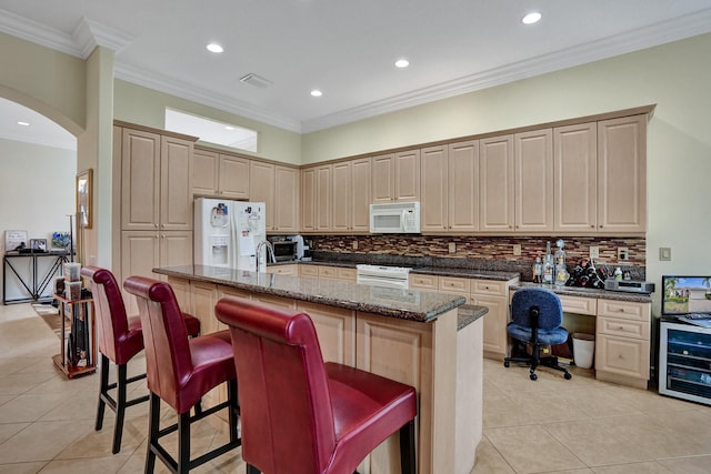 kitchen with white appliances, beverage cooler, a kitchen island with sink, a kitchen bar, and dark stone counters