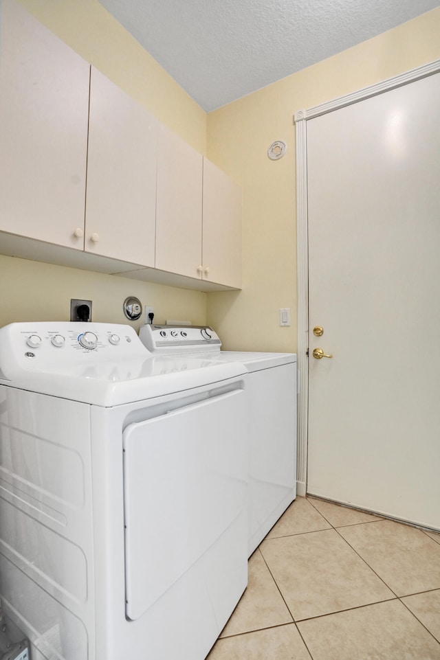 laundry area with a textured ceiling, cabinets, washer and clothes dryer, and light tile patterned flooring