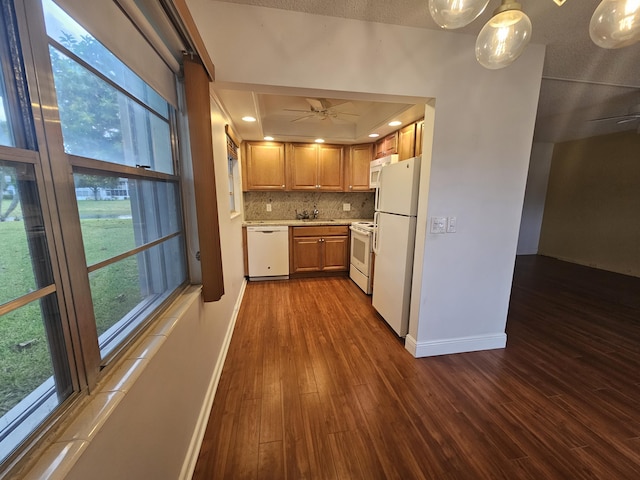 kitchen with white appliances, a tray ceiling, tasteful backsplash, dark wood-type flooring, and ceiling fan