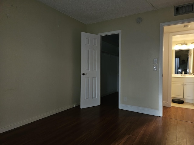 unfurnished bedroom featuring ensuite bath, dark wood-type flooring, and sink