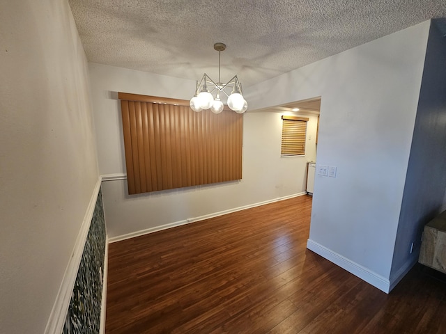 empty room featuring a textured ceiling, dark hardwood / wood-style floors, and an inviting chandelier