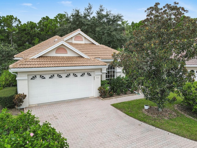 view of front facade with a tiled roof, stucco siding, an attached garage, and decorative driveway