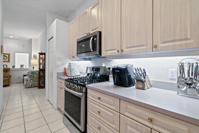 kitchen with stainless steel appliances, light tile patterned floors, backsplash, and light brown cabinetry